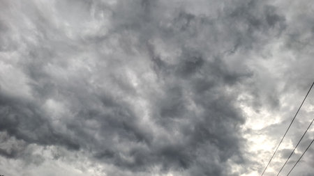 A dramatic view of a dark, overcast sky filled with thick storm clouds, indicating the coming of...
