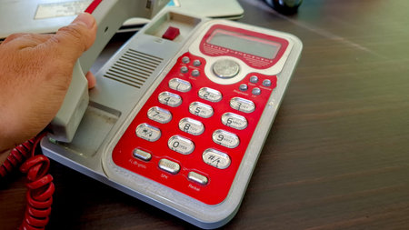 close-up of someone picking up a red and gray landline telephone, which is placed on a dark wooden...