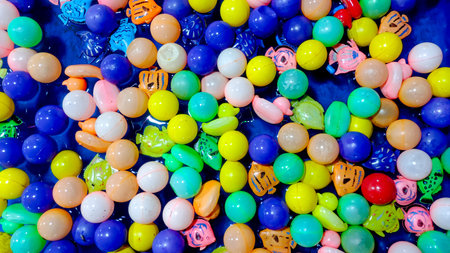 Overhead photograph of vibrant plastic balls and colorful toy fish floating on a blue water surface.