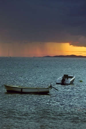 Two boats with sunset and rain's clouds on seaの写真素材