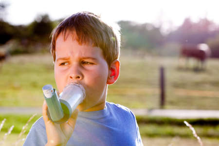 Boy using inhaler for asthma in village with cows and sunsetの写真素材