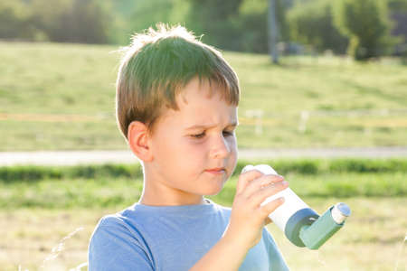 Boy using inhaler for asthma in village with summer sunsetの写真素材