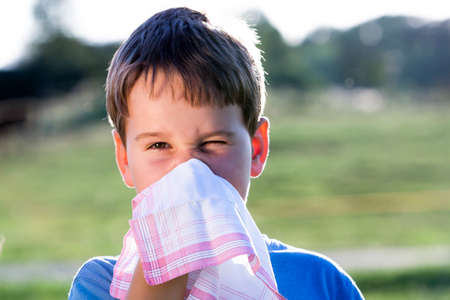 child with an allergy to pollen while you blow your nose with a white handkerchief in natureの写真素材