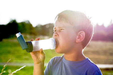 Boy using inhaler for asthma in village with summer sunsetの写真素材
