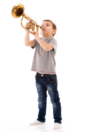 young boy blowing into a trumpet against white background
