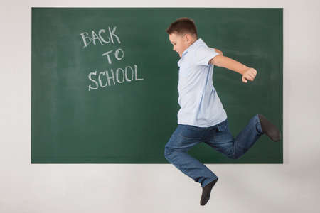 Young boy jumping in a green chalkboard with the words back to schoolの写真素材