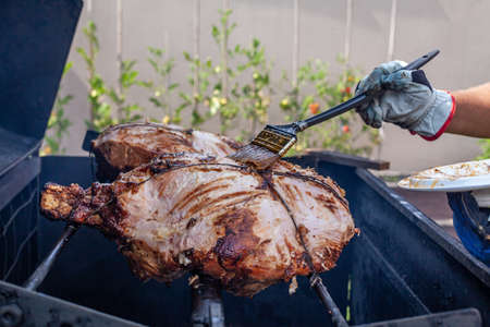 Man hand grilling barbecue with big pork at backyard on day. Family dinner outdoor style bbq activity.の写真素材