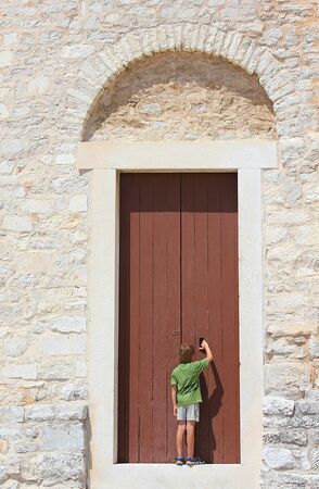 a young curious boy standing before an old doorの写真素材