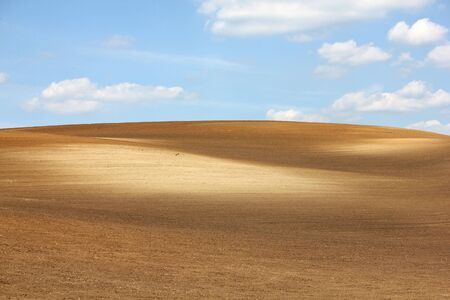 Colorful brown arable hill against cloudy blue skyの写真素材