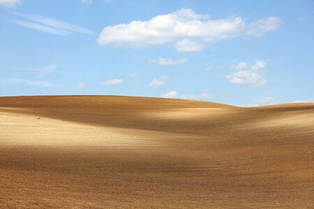 Colorful brown hills arable against cloudy blue skyの写真素材