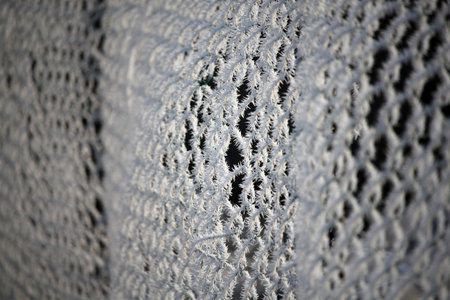 Frosty metal fence covered with morning frost in beautiful winter sunshine. Selective focus with...