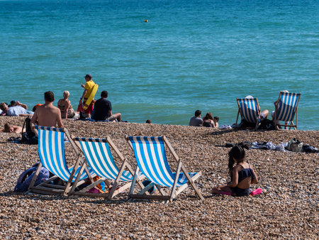 BRIGHTON, UK - SEPTEMPER 1, 2018: Three deck chairs and a little girl on the beachのeditorial素材