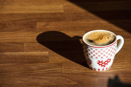 cup of coffee on a wooden deskwith the early morning light and long shadowsの写真素材