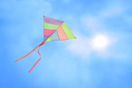 angle view of a colorful kite flying with waving red bow in a deep blue sky with the light of the sunの写真素材