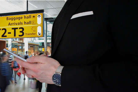 A close up view of a business man in a black suit holding a smartphone in an airport