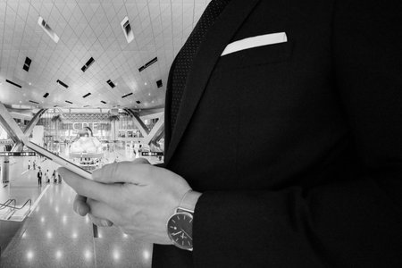 A close up view of a business man in a black suit holding a smartphone in a train station