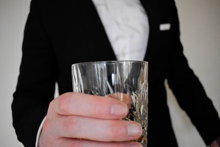 A close up view of a man in a black tuxedo cheersing with a whiskey glassの写真素材