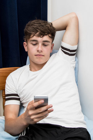 Teenage boy using a phone in his bedroomの写真素材