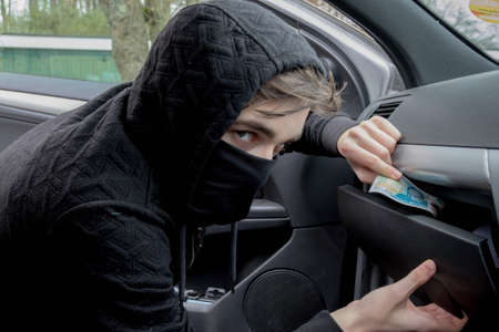 Masked teenage criminal stealing from a carの写真素材
