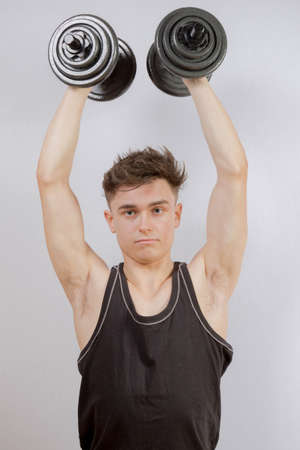 Strong teenage boy exercising by lifting weightsの写真素材