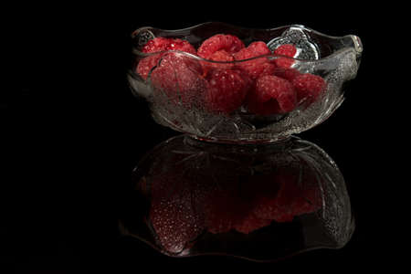 Raspberries in a glass bowl isolated on a black backgroundの写真素材