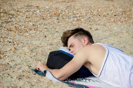Teenage boy laying on a stoney beachの写真素材