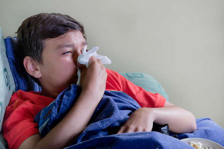Unwell young teenage boy wrapped in a duvet on a sofaの写真素材