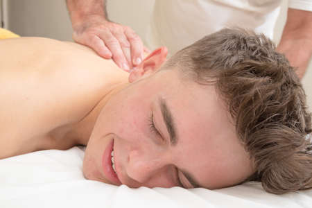 Teenage boy laying on a massage table, having a back massageの写真素材