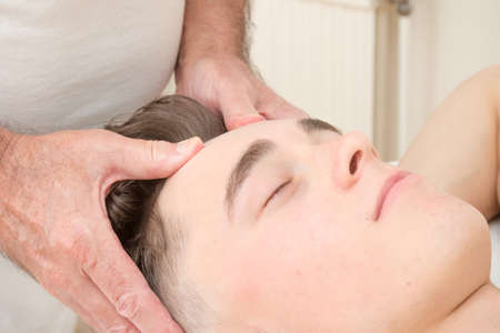 Teenage boy laying on a massage table, having a head massageの写真素材