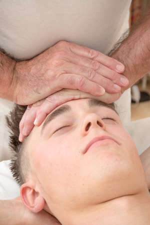 Teenage boy laying on a massage table, having a head massageの写真素材