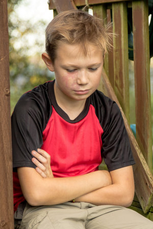 Sad pre-teen boy sitting outside on a climbing frame