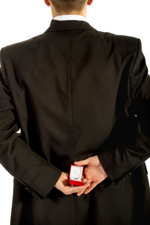 18 year old wearing a tuxedo hiding a ring box behind his back isolated on a white background