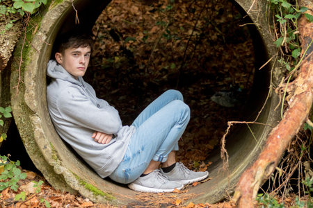 Teenage boy sitting in an old drainage pipe on an autum day