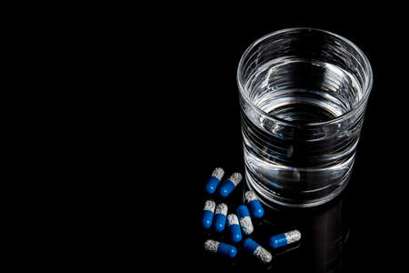 Medical pills next to a glass of water isolated  on a black backgroundの写真素材