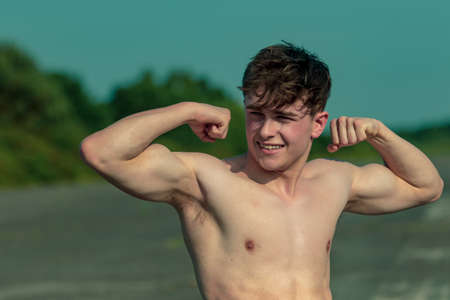 Young adult male flexing his muscles shirtless on a warm summer's dayの写真素材