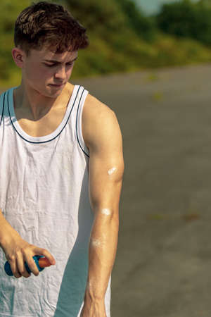 Young adult male putting on sun cream outside in the sunshineの写真素材