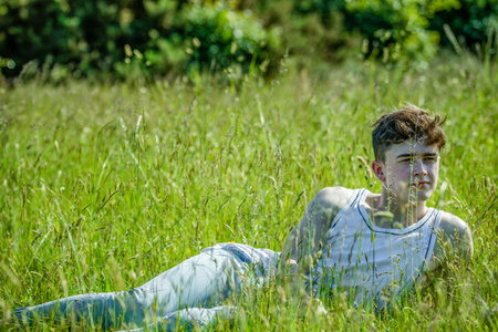 A young adult male laying amoung long grass on a warm summer's day