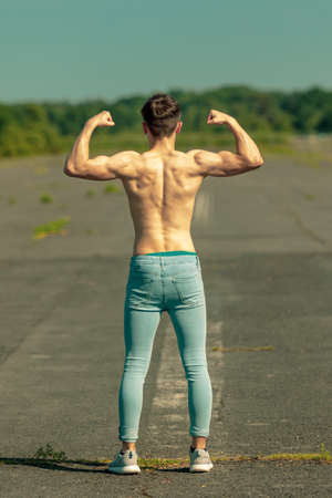 Young adult male flexing his muscles viewed from the back on a warm summer's dayの写真素材