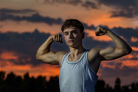 Young male adult flexing his arm  muscles at sunsetの写真素材
