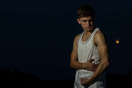 Young male adult outside flexing his arms with the moonの写真素材