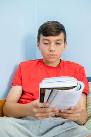 Caucasian teenage boy reading a book laying on a bed