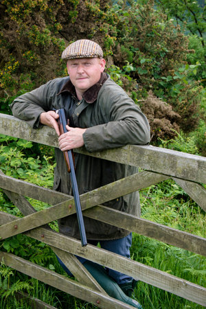 Farmer leaning on a wooden gate holding a broken shotgun