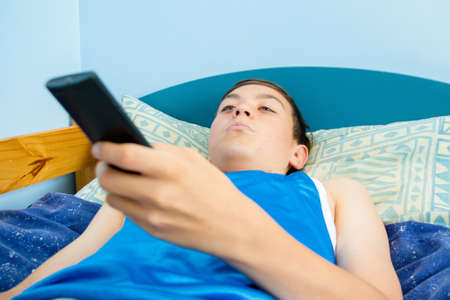 Caucasian teenage boy flicking through tv channels with a remote controlの写真素材