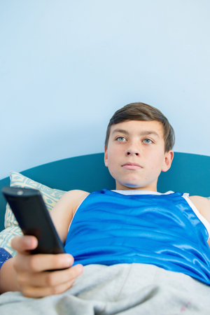 Caucasian teenage boy flicking through tv channels with a remote control
