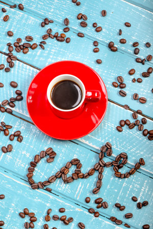 Espresso cup of coffee with the word cafe spelt with coffee beans on a wooden background