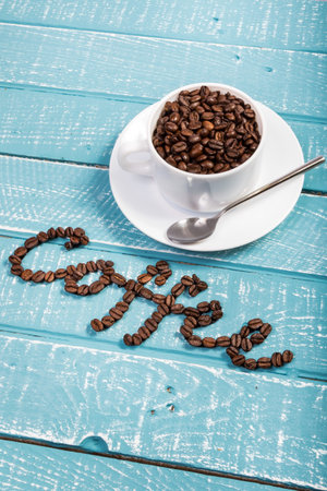 A cup filled with coffee beans on a weathered table with the word coffeeの写真素材