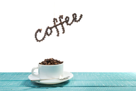 A cup filled with coffee beans on a weathered table with the word coffee above with a white...