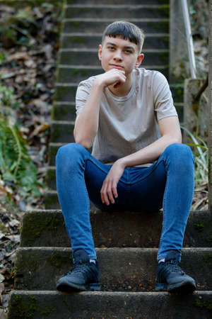 Portrait of a caucasian teenage boy sitting outside on concrete stepsの写真素材
