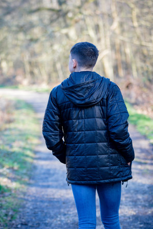 Caucasian teenage boy walking away wearing a jacket on a spring day