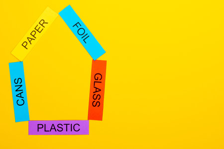Recycling concept showing paper, foil, cans, glass & plastic on a yellow background